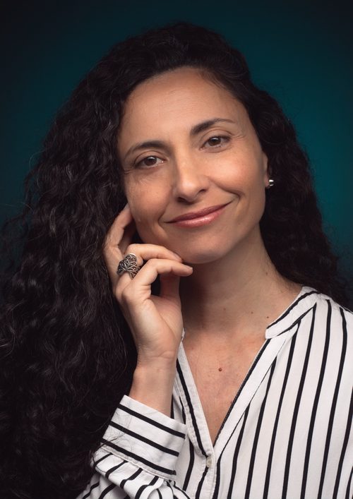 Professional headshot of a smiling businesswoman with a slight head tilt and hand resting lightly against her face