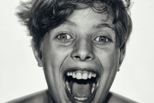 High-key black and white close-up portrait of a boy with his mouth open, facing the camera.