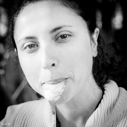 Black and white portrait of a woman eating from a spoon while looking intently at the camera.