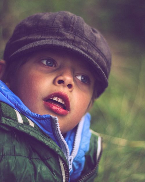 Close portrait of a young boy wearing a hat, looking off into the distance in soft, faded colors.